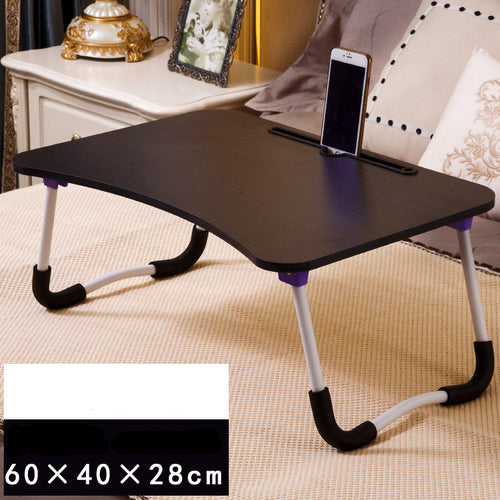 Foldable laptop desk on a bed with a phone on top, surrounded by pillows and a cabinet.