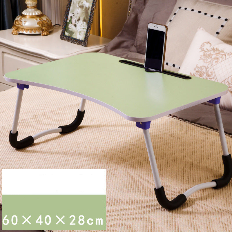 Foldable laptop desk with a phone stand on a bed, surrounded by decorative items.